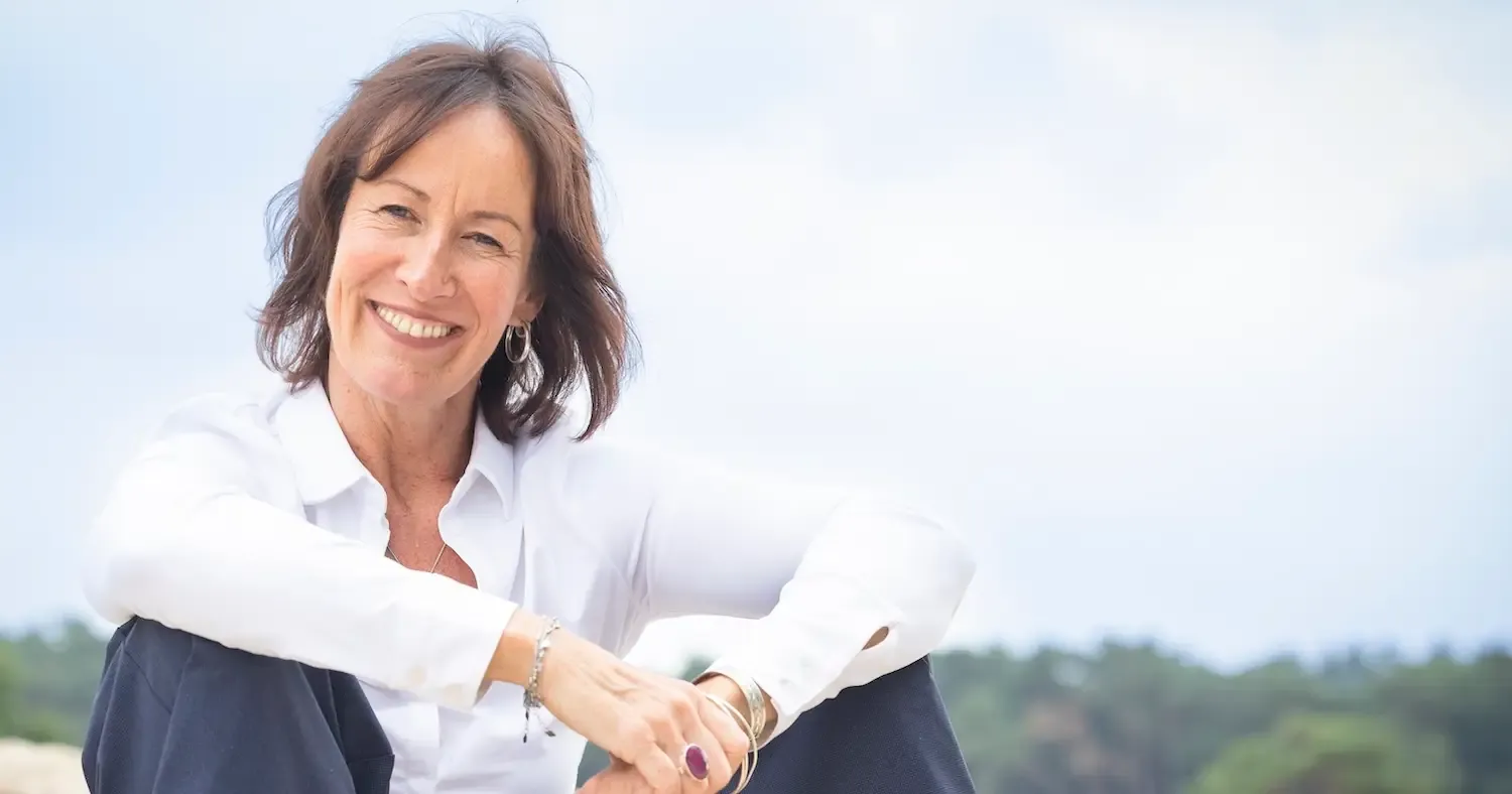 Jacqueline Lammerts, relatiecoach, zit lachend in een witte blouse onder een open lucht
